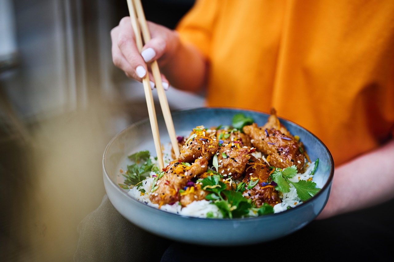 A bowl of glazed crispy chicken on rice with spring onion, eaten with chopsticks